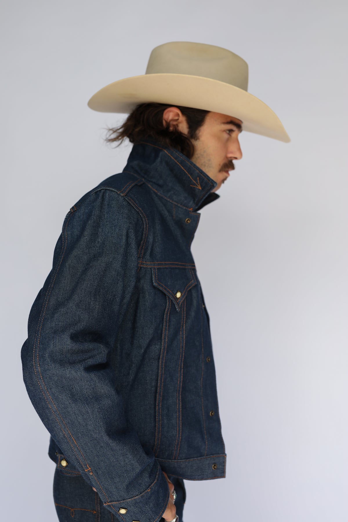 Side view of the H Bar C Salina indigo denim jacket with collar up and a cowboy hat.