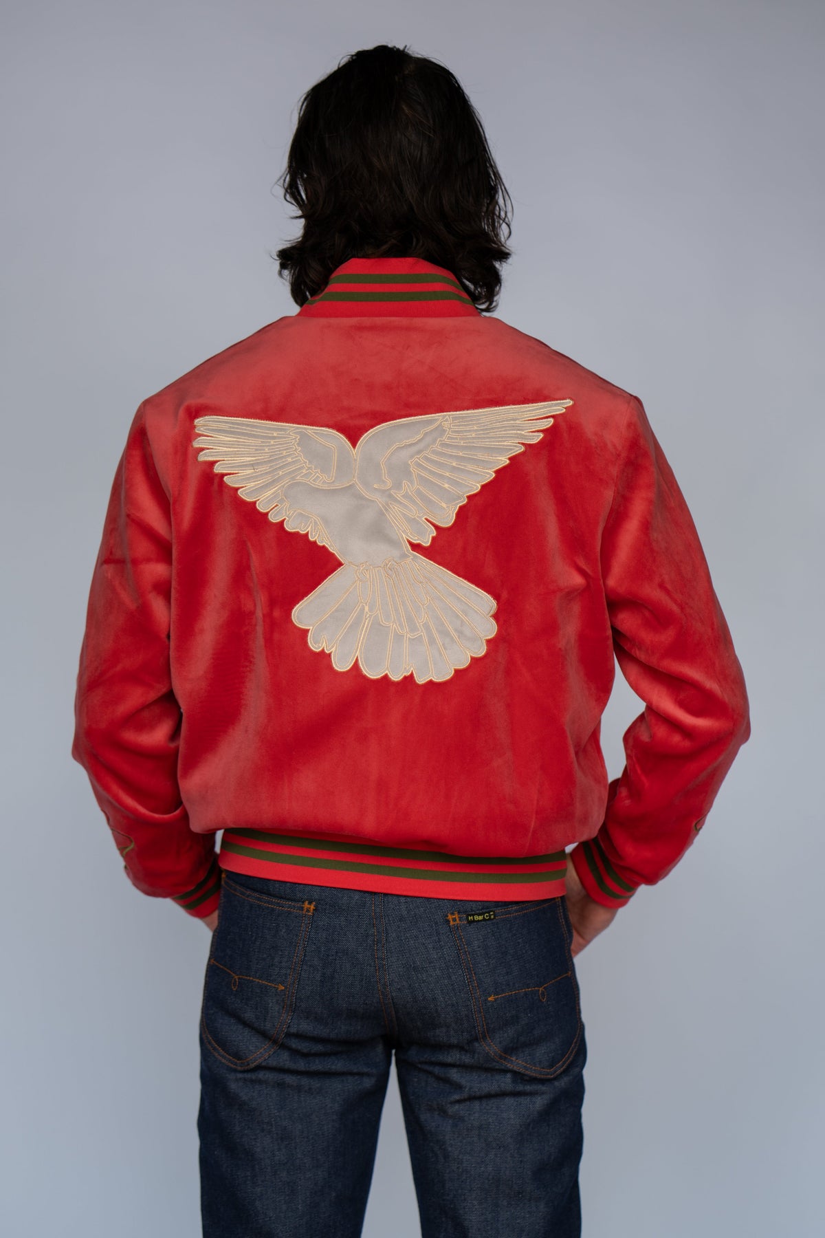 Back view of a man wearing the HBarC x Gibson Dove red tour jacket with the dove back embroidery and jeans.