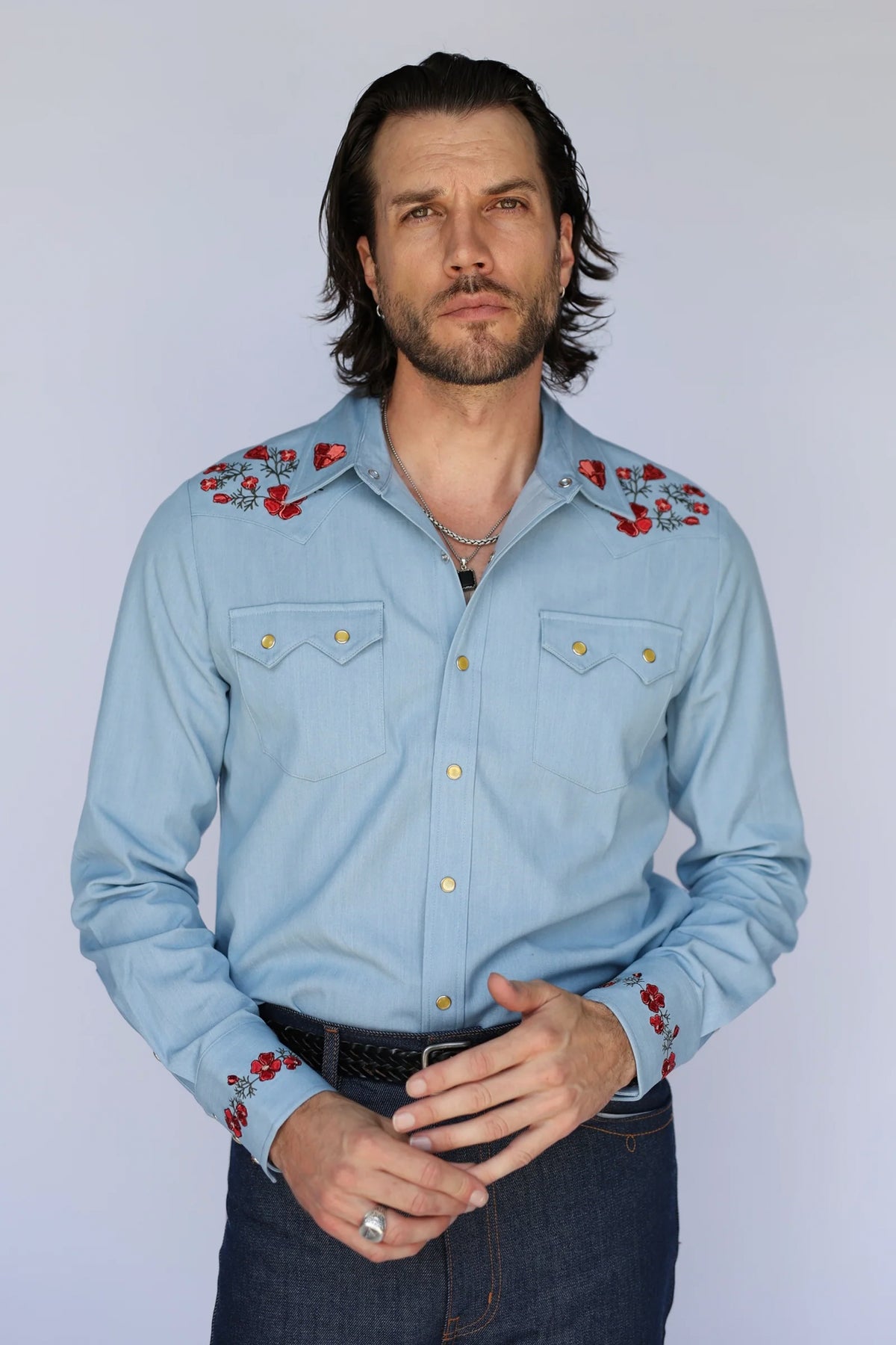 Man wearing the HBarC x Gibson Dove shirt, a light blue chambray pearl snap western shirt with red poppy embroidery inspired by the Gibson Dove guitar.