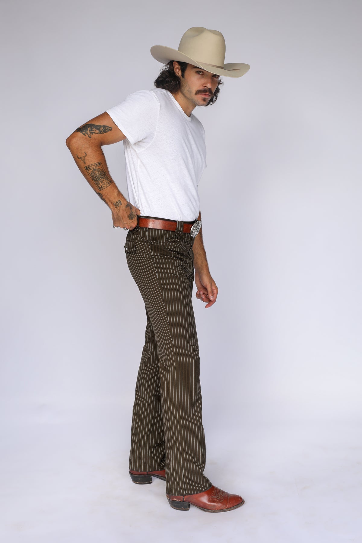 Three-quarter view of the H Bar C Bakersfield brown pinstripe pants styled with a white tee and cream cowboy hat.