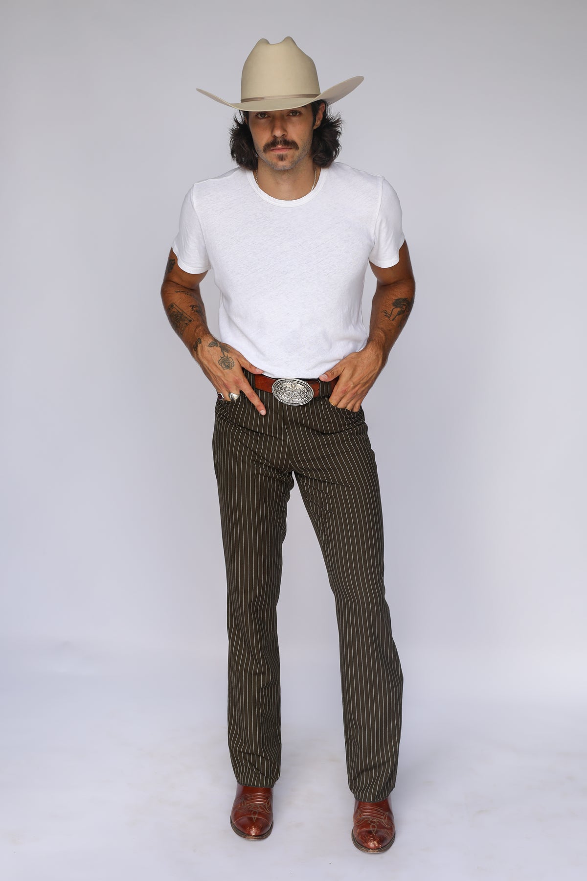 Full front view of the H Bar C Bakersfield brown pinstripe western pants styled with a white tee, cowboy hat, and boots.