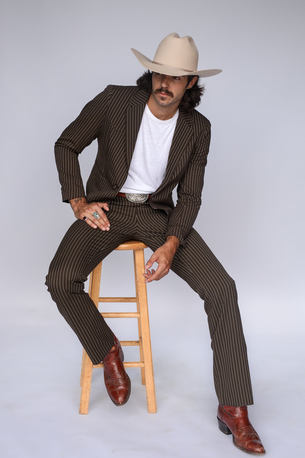 Seated pose in the H Bar C Bakersfield brown pinstripe suit with white tee, cowboy hat, and boots.