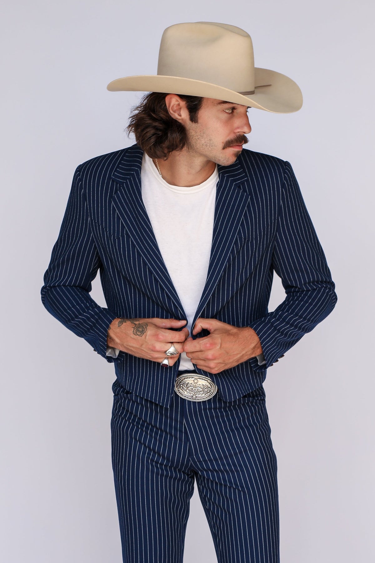 Man buttoning the H Bar C Bakersfield navy pinstripe jacket worn with matching pants and a cowboy hat.