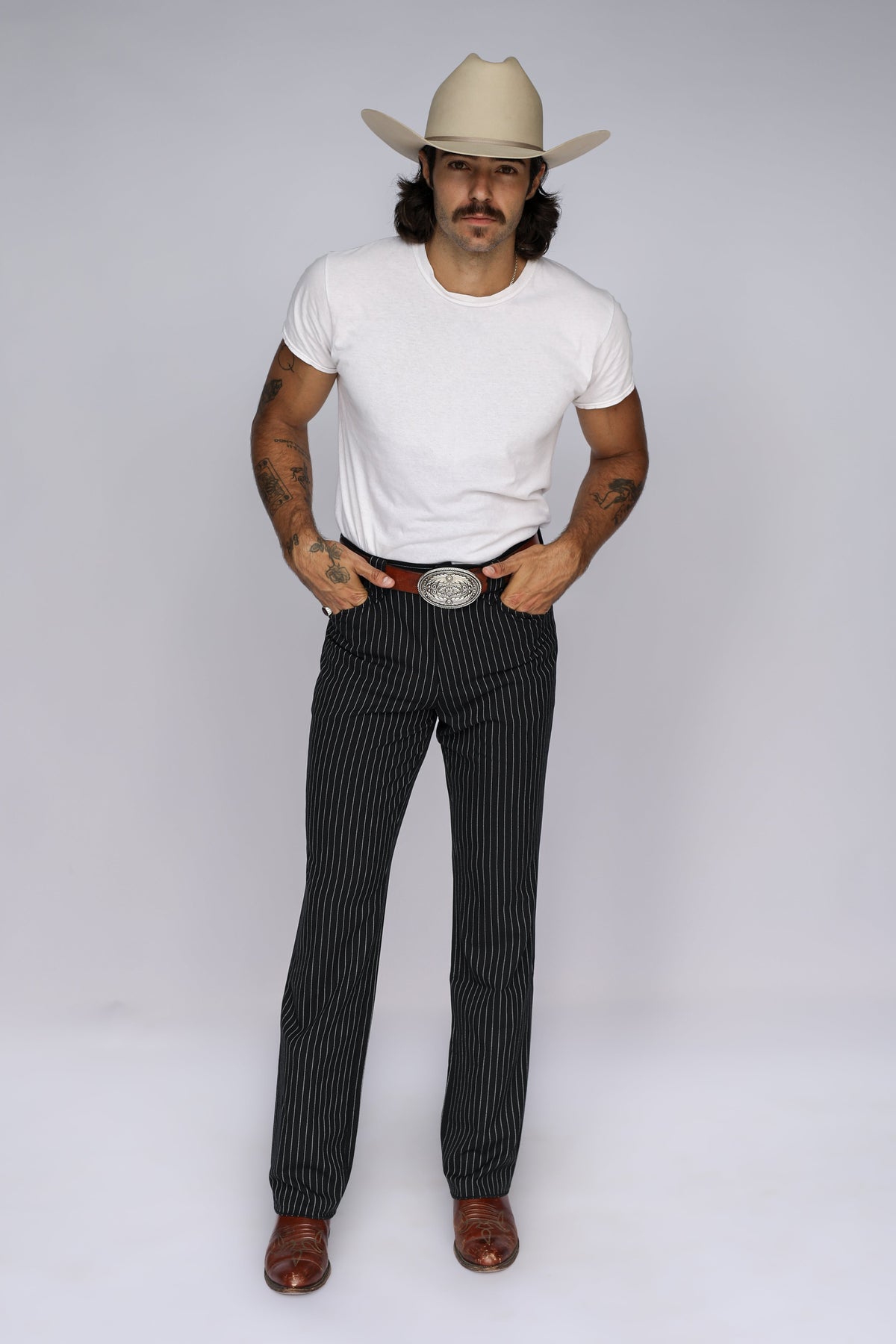 Man in a cream cowboy hat wearing the H Bar C Bakersfield black pinstripe western pants with a white tee and buckle.