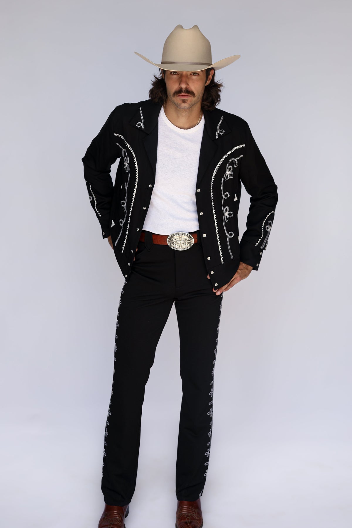 Man wearing the H Bar C Bolero black jacket and matching embroidered Bolero pants, the Bob Wills inspired western suit, with a white tee and silver buckle.