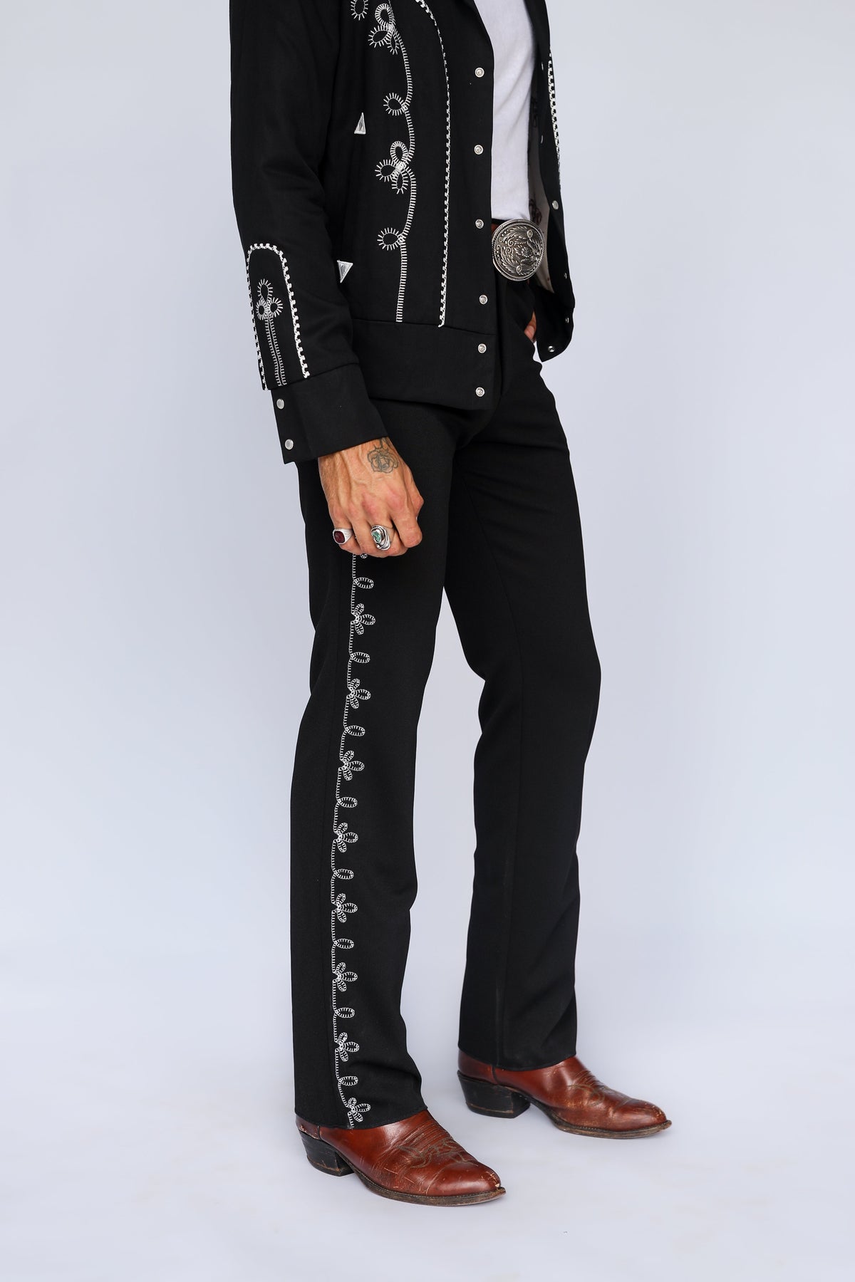 Side leg detail of the H Bar C Bolero pants in black with white chain stitch embroidery down the leg, worn with cowboy boots.