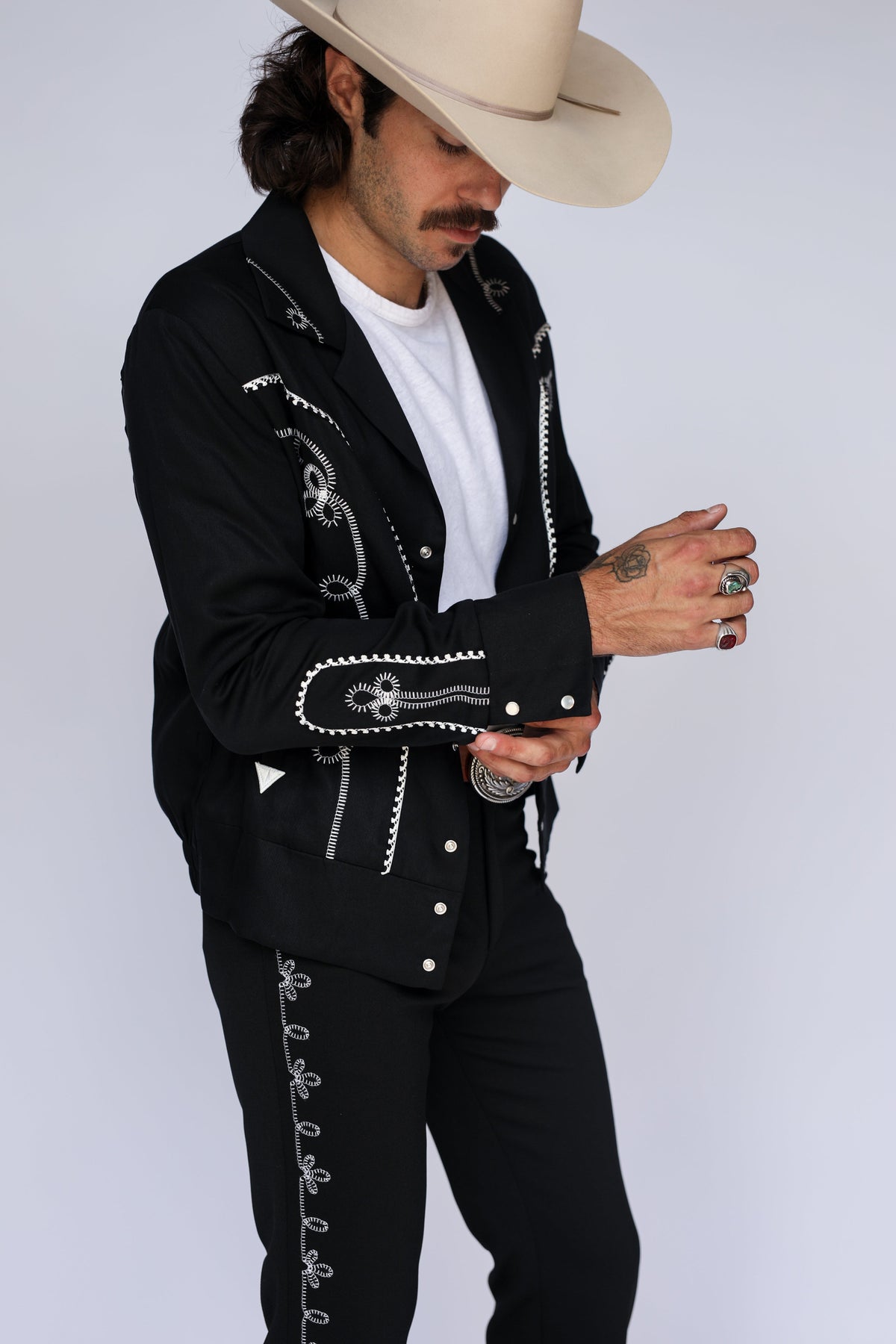 Model buttoning the cuff of the H Bar C Bolero black and white jacket, styled with the matching embroidered Bolero pants and a cream cowboy hat.