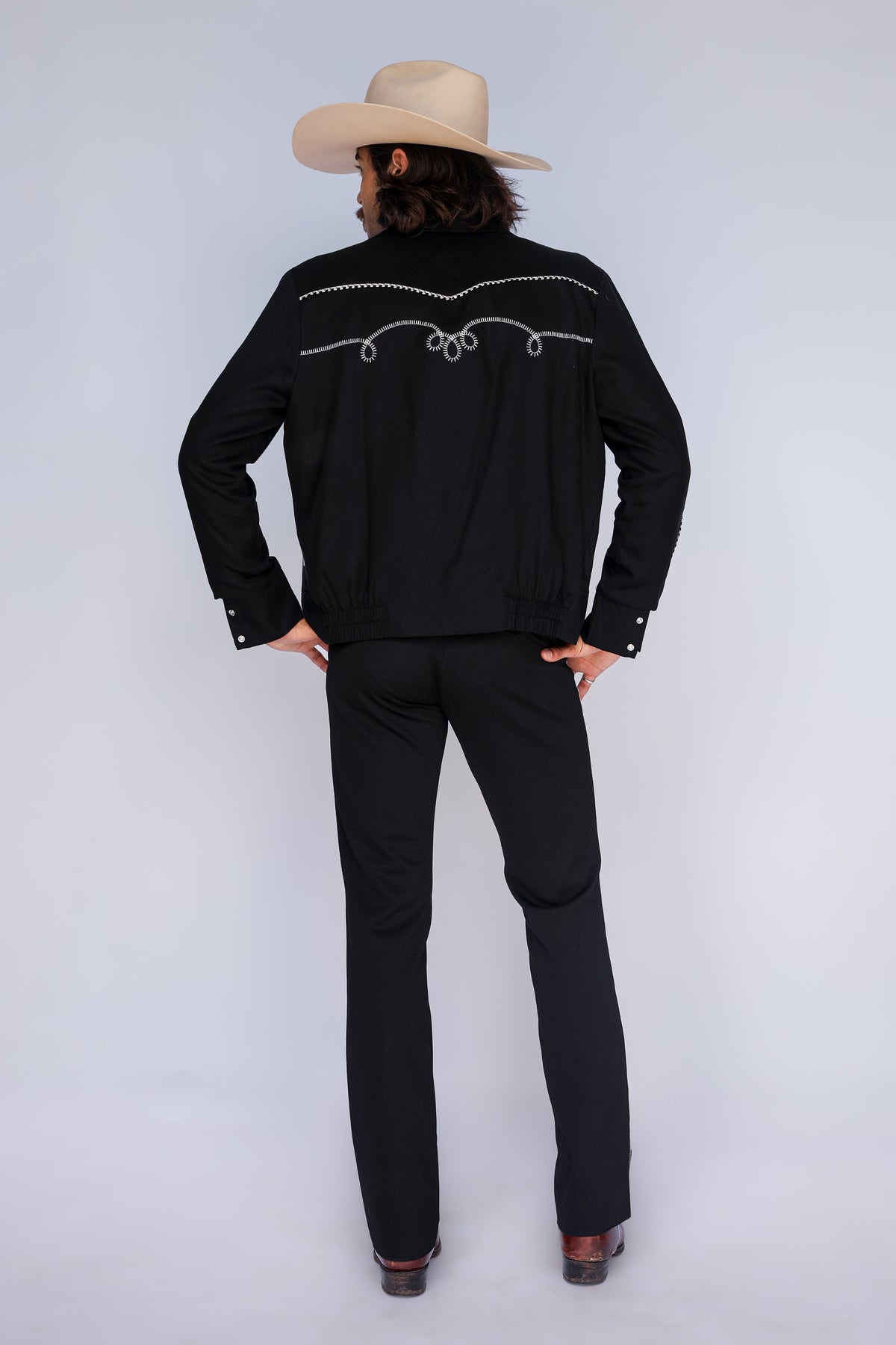 Back view of the H Bar C Bolero men's black jacket with white embroidered back yoke, worn with Bolero pants and a cowboy hat.