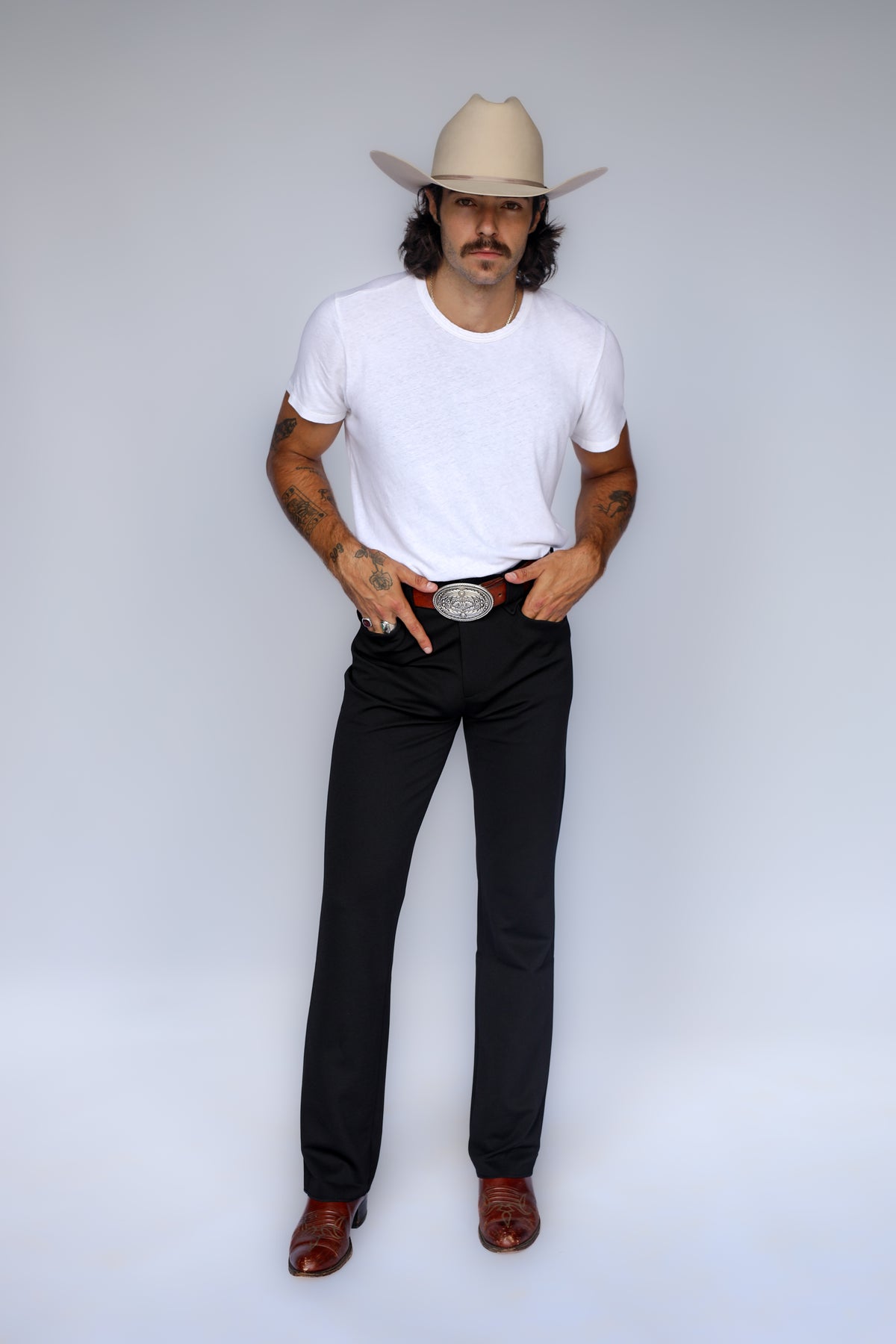 Man wearing the H Bar C Franklin unisex black western pants with a white tee, silver buckle, cowboy hat, and boots.