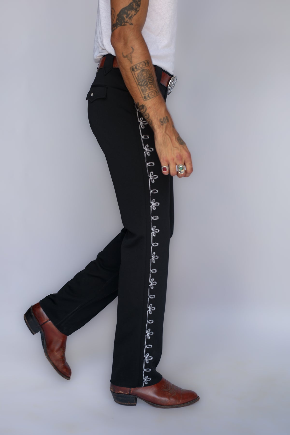 Side view in stride of the H Bar C Bolero black pants showing the embroidered leg detail and cowboy boots.