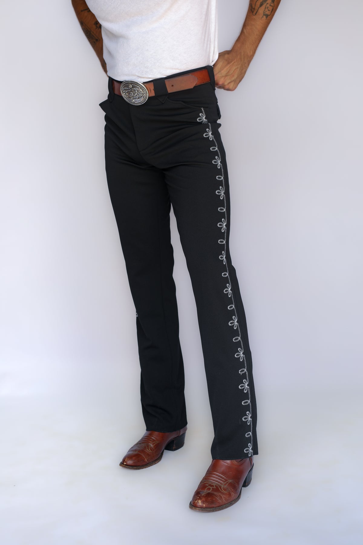 Three-quarter view of the H Bar C Bolero pants in black with embroidered side stripe, silver buckle, and cowboy boots.