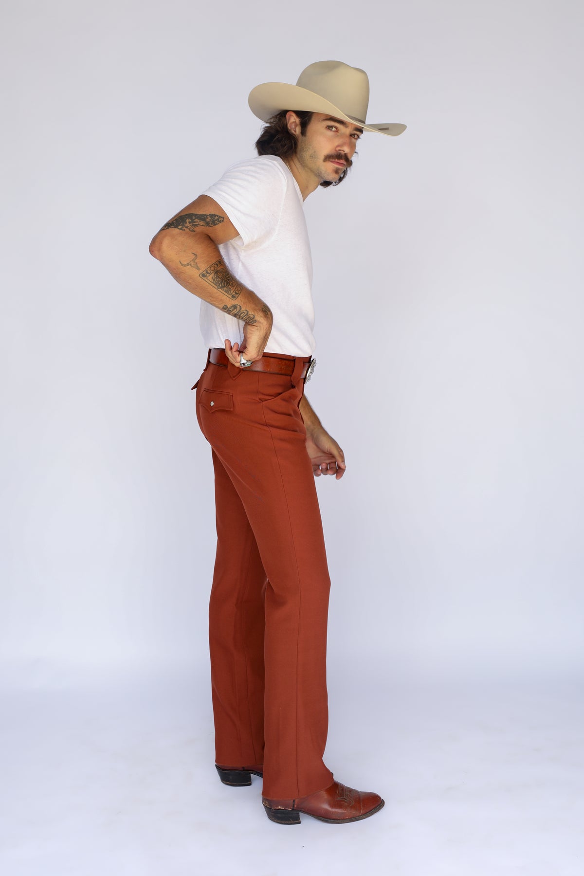 Side view of a man adjusting his hat in the H Bar C Franklin brown western pants.