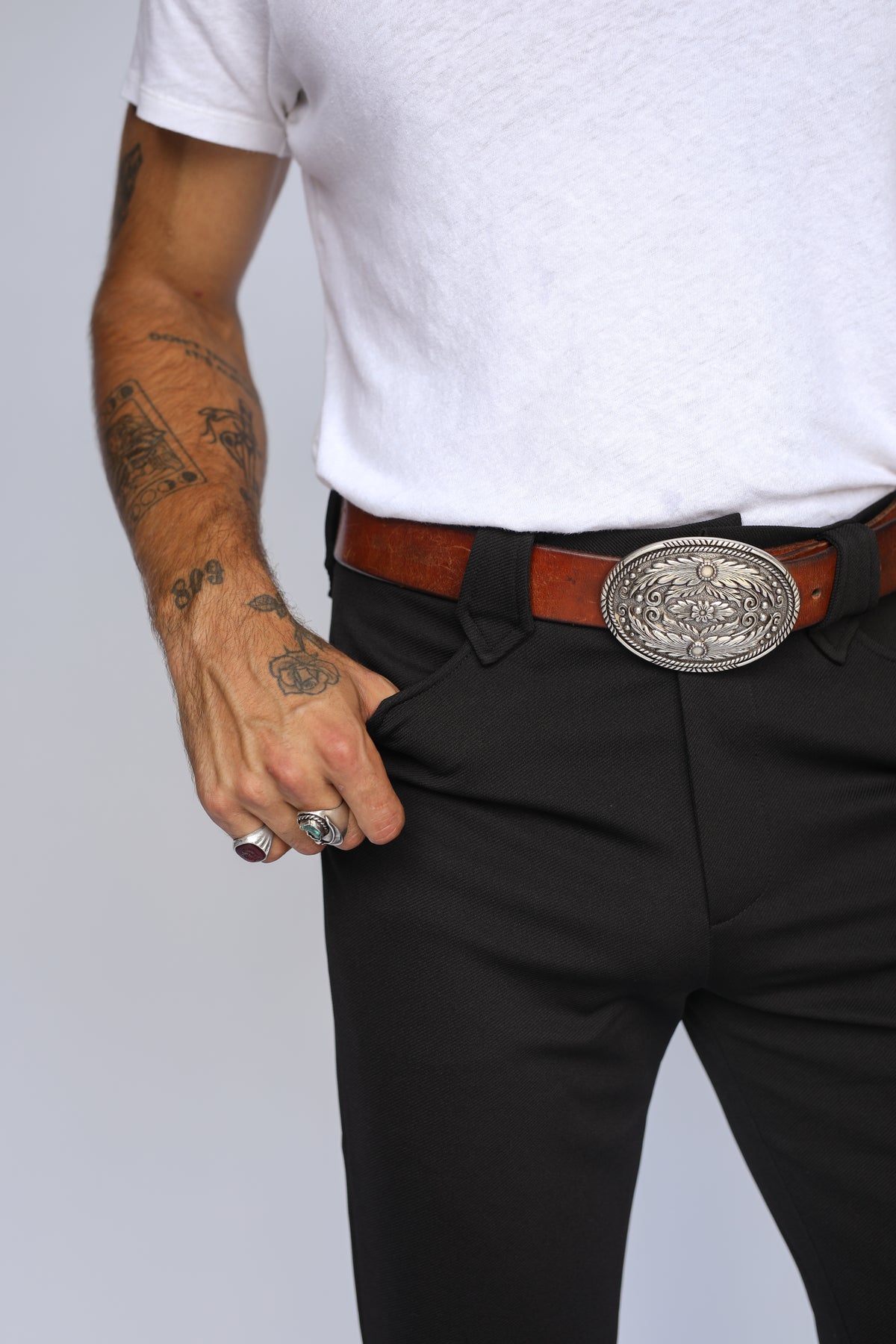 Front waist detail of the H Bar C Franklin black western pants worn with a brown belt and engraved silver buckle.