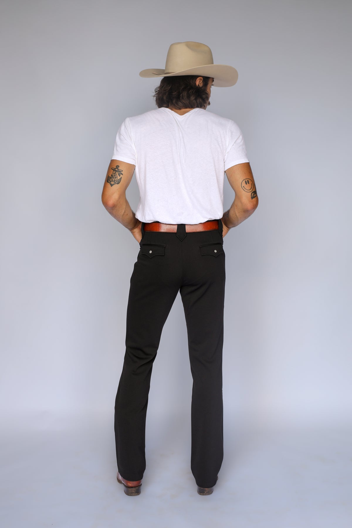 Back view of the H Bar C Franklin black western pants styled with a white tee, brown belt, and cowboy hat.