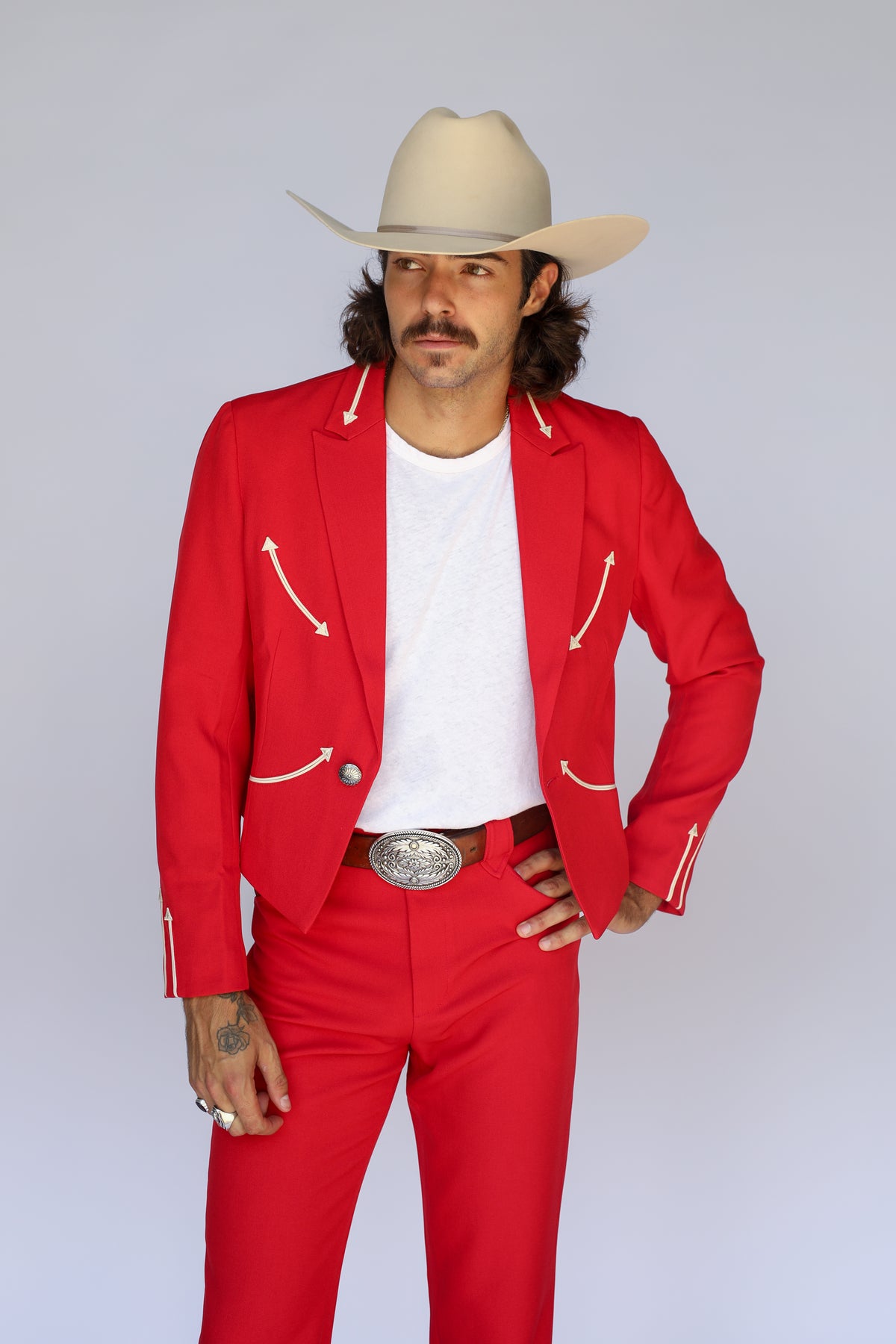 Man in a cream cowboy hat wearing the H Bar C Calamity men's jacket in red with cream arrow details and matching red western pants.