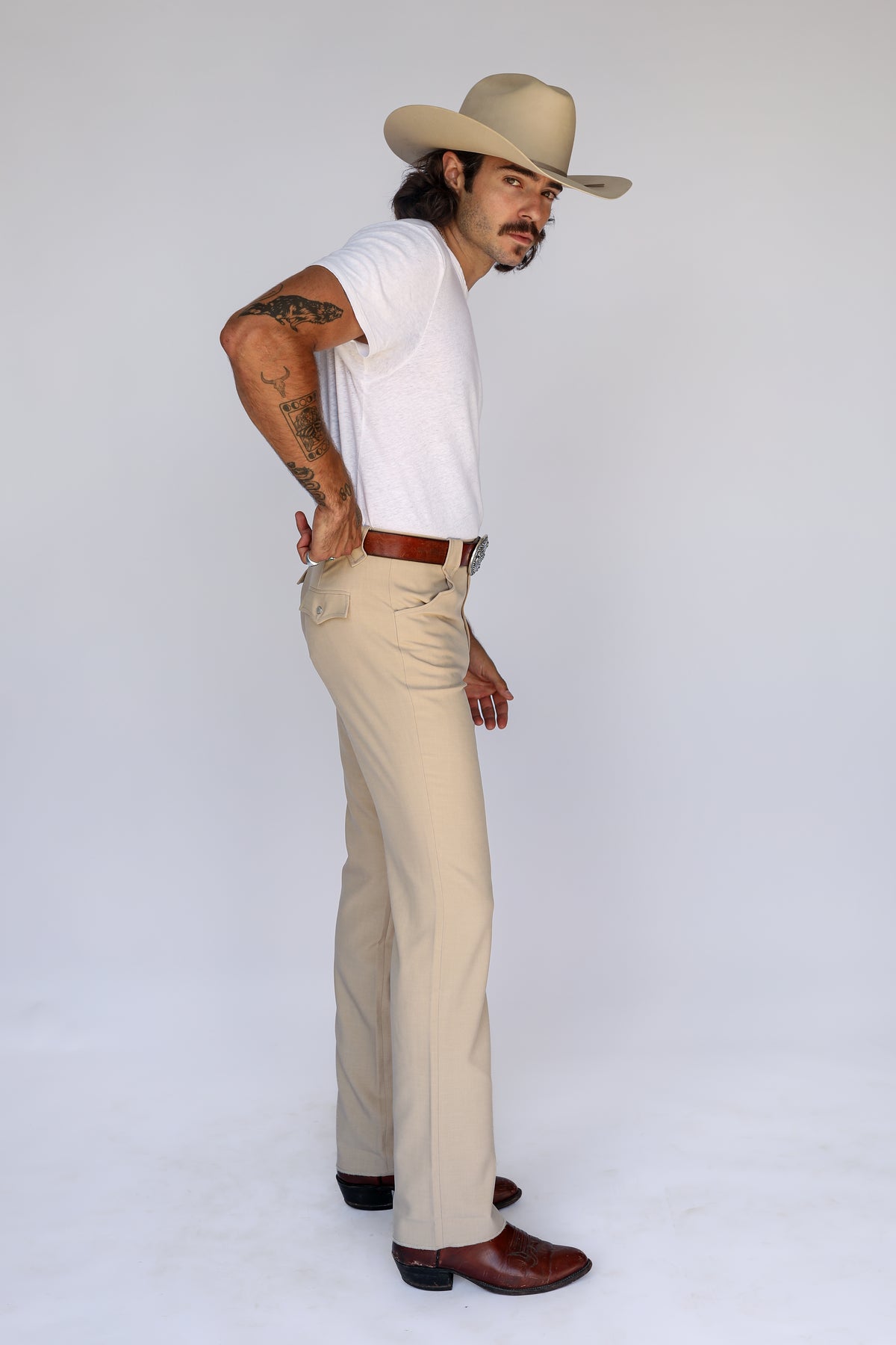 Side profile of the H Bar C Calamity tan pants with a white tee and cowboy hat.