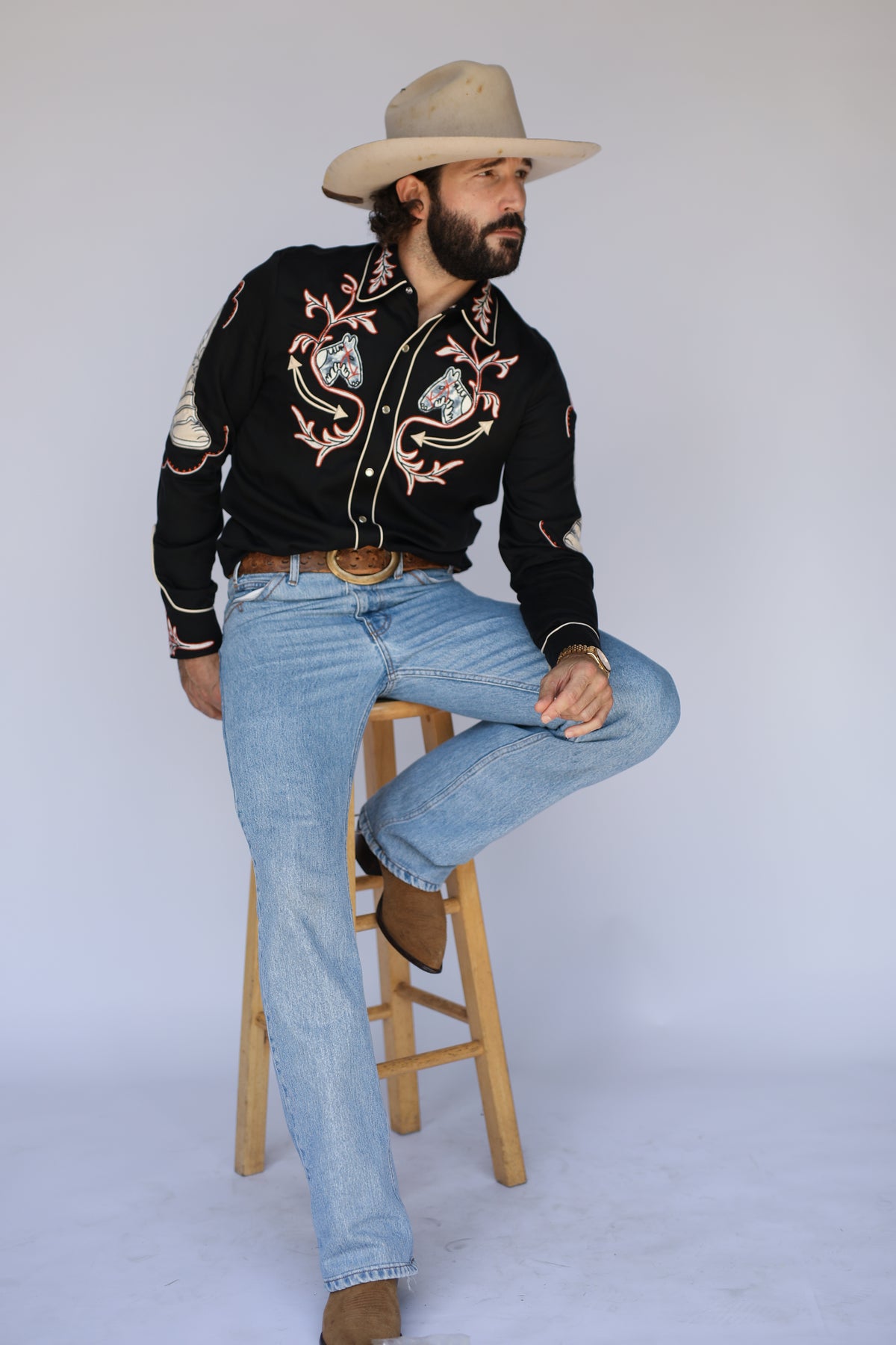 Seated pose in the H Bar C Calabasas black embroidered western shirt with a straw hat.