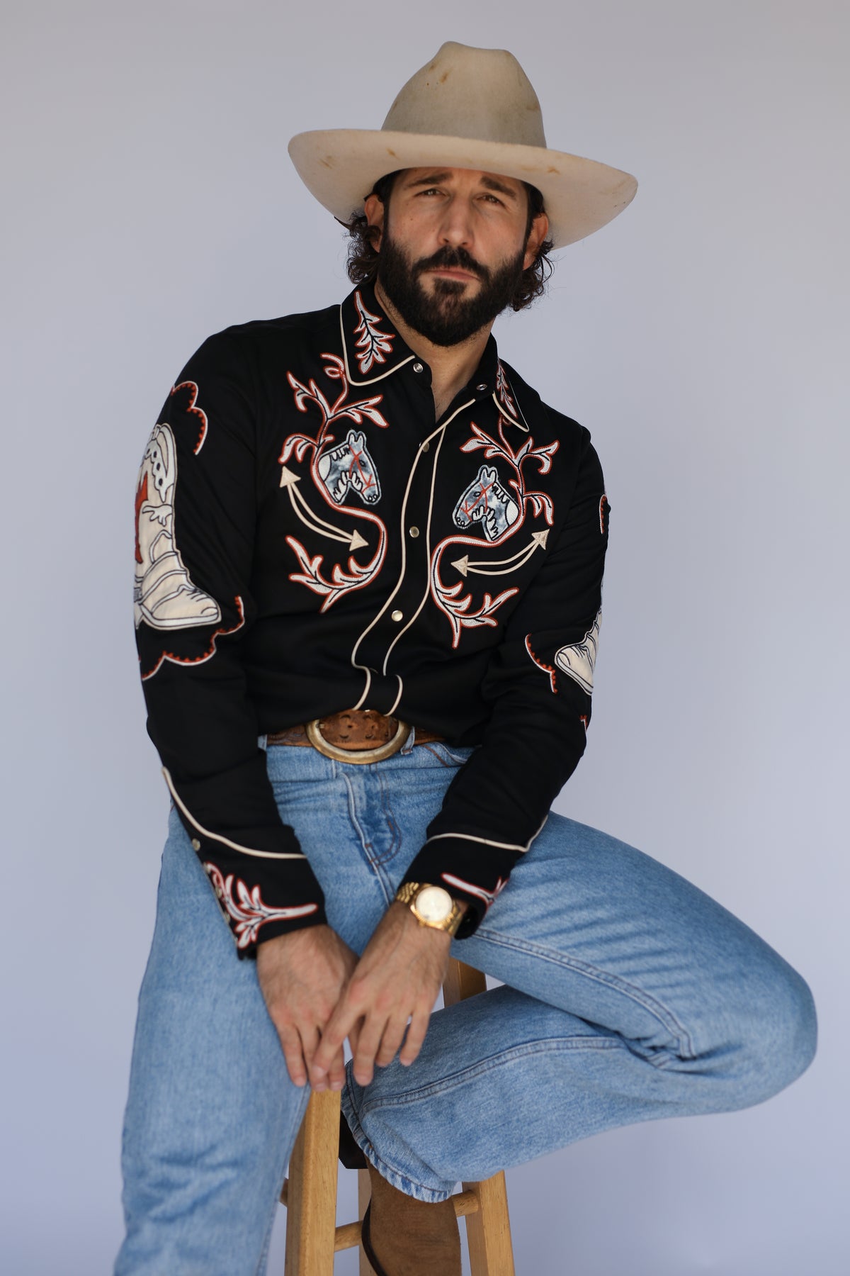 Man seated wearing the H Bar C Calabasas black shirt showing horse head and cactus embroidery.