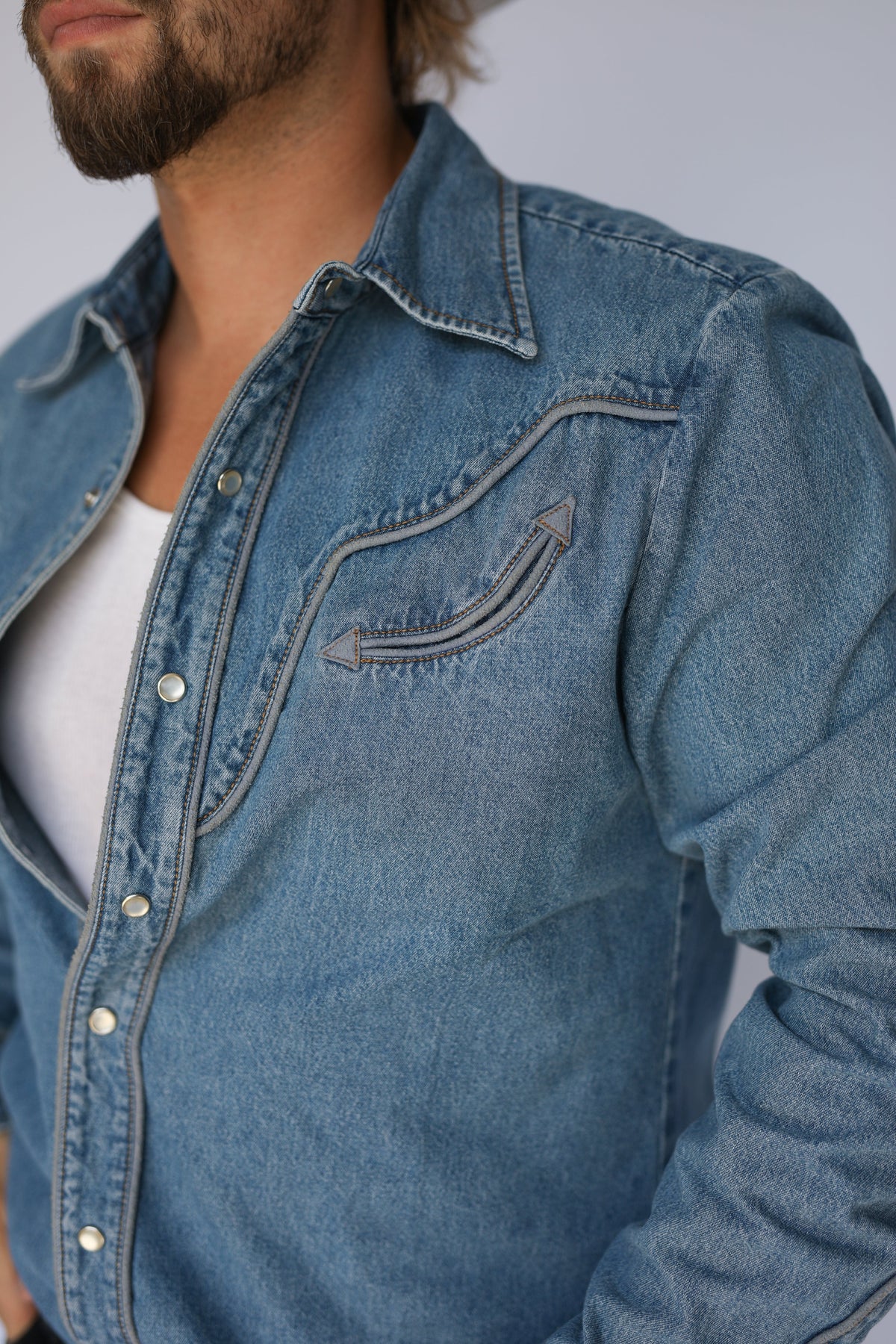 Close-up of the H Bar C San Fernando denim western shirt showing contrast stitched smile pocket over a white undershirt.