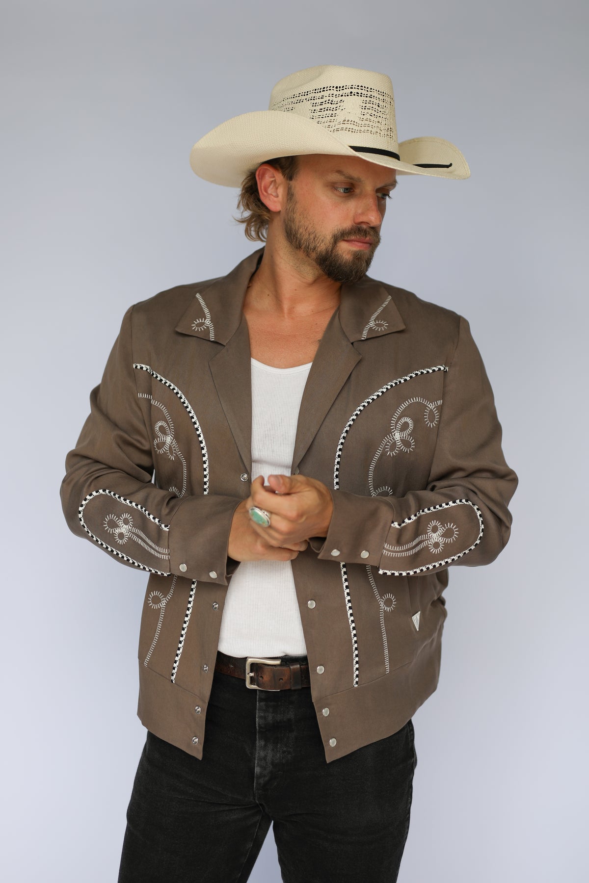 Man in a straw cowboy hat wearing the H Bar C Bolero men's jacket in cocoa and white with chain stitch embroidery, the 1936 Bob Wills design.