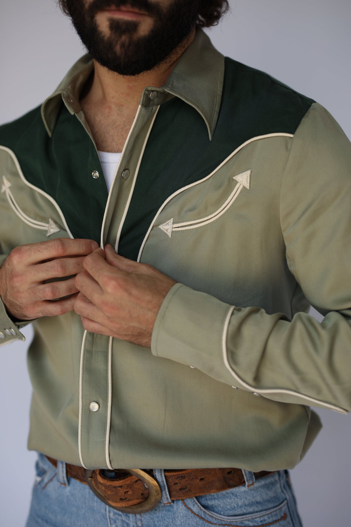 Close-up of the cream arrow-tipped smile pocket, piping, and pearl snaps on the H Bar C San Juan green western shirt.