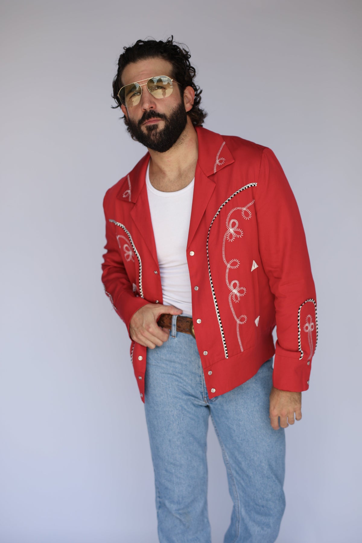 Man in aviator sunglasses wearing the H Bar C Bolero red jacket with white chain stitch details.