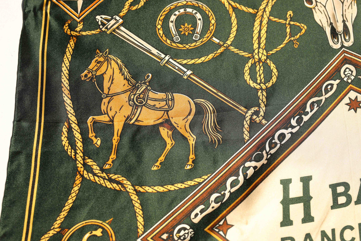 Detail of a saddled palomino horse, spur, and horseshoe medallion on the H Bar C Green silk scarf, a classic western ranch print.