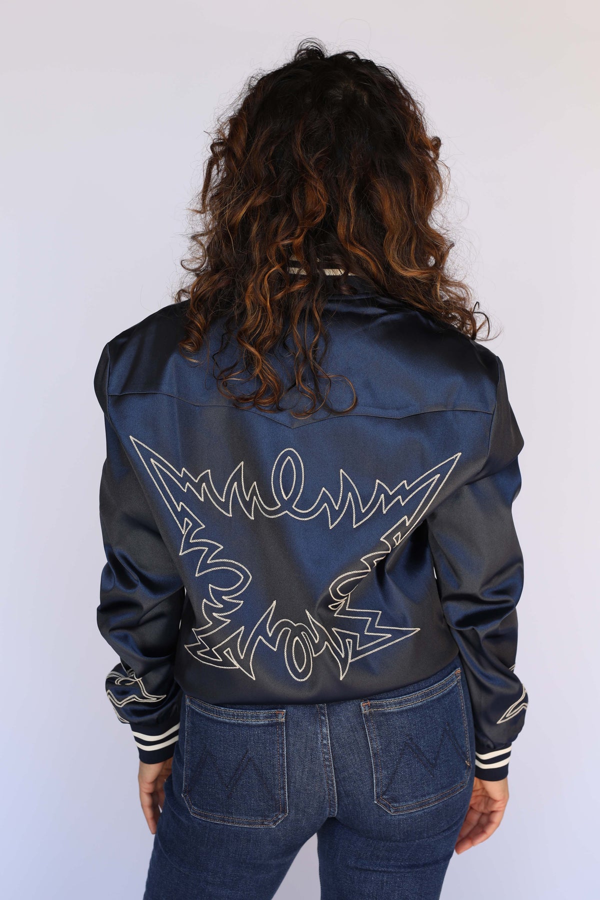 Back view of the H Bar C Odessa navy satin tour jacket with cream chain stitch embroidery on a female model.