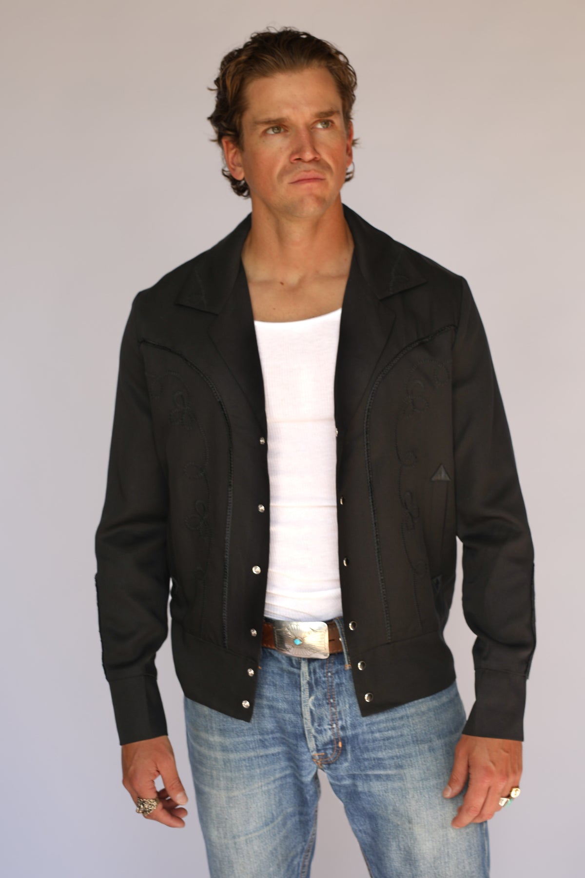 Man wearing the H Bar C Bolero black on black jacket open over a white tank and jeans.