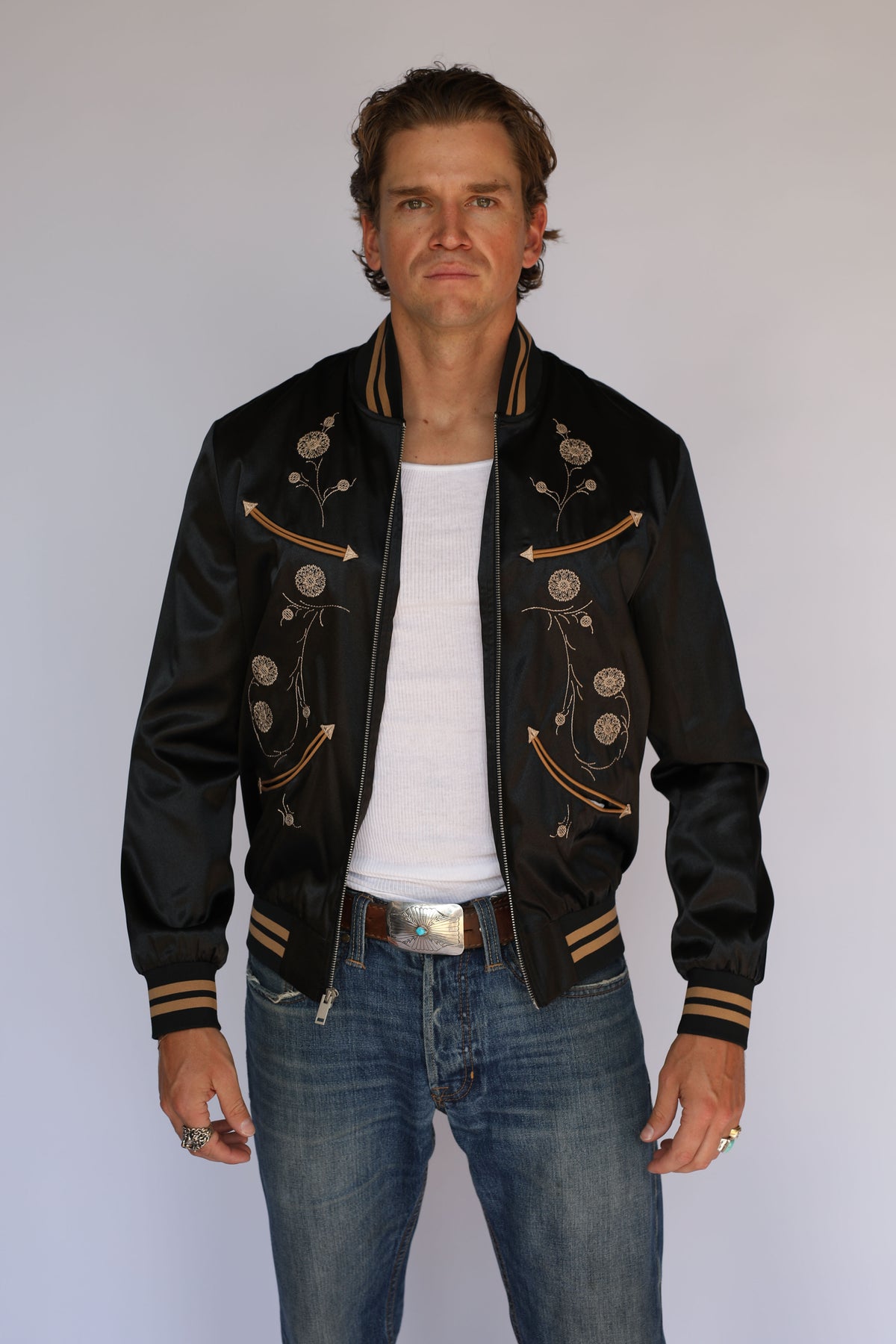 Man in the open H Bar C x Gibson Odessa black satin bomber jacket, vintage western wear with embroidered front panels and striped cuffs.