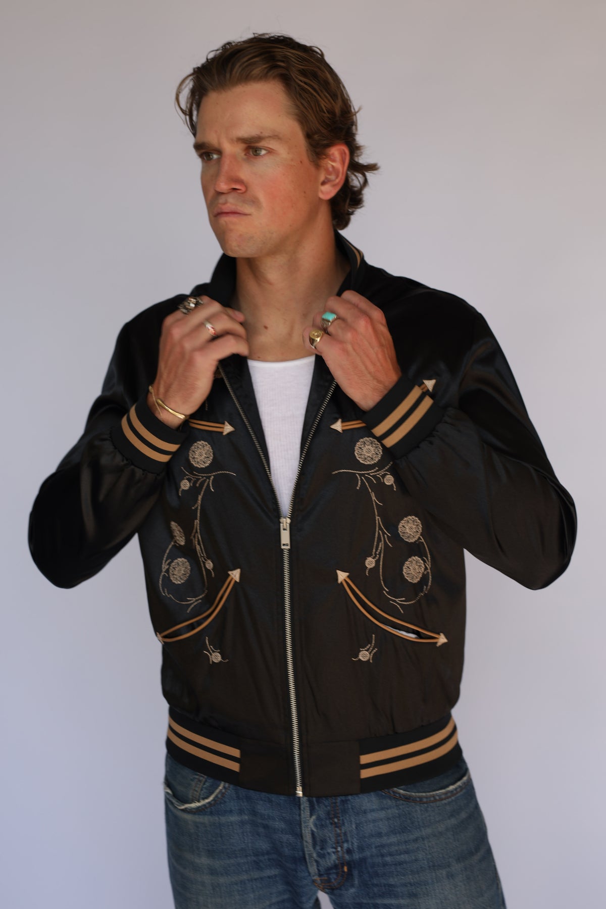 Model adjusting the H Bar C x Gibson Odessa black satin jacket, vintage western wear with tan and black striped ribbed collar.