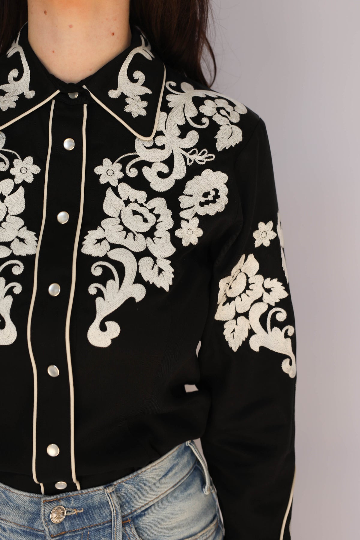 Close-up of the H Bar C Fort Worth black twill shirt with ivory chain stitch floral and scroll embroidery on the collar, yoke, and sleeve, piped placket, and pearl snaps, vintage inspired western wear.