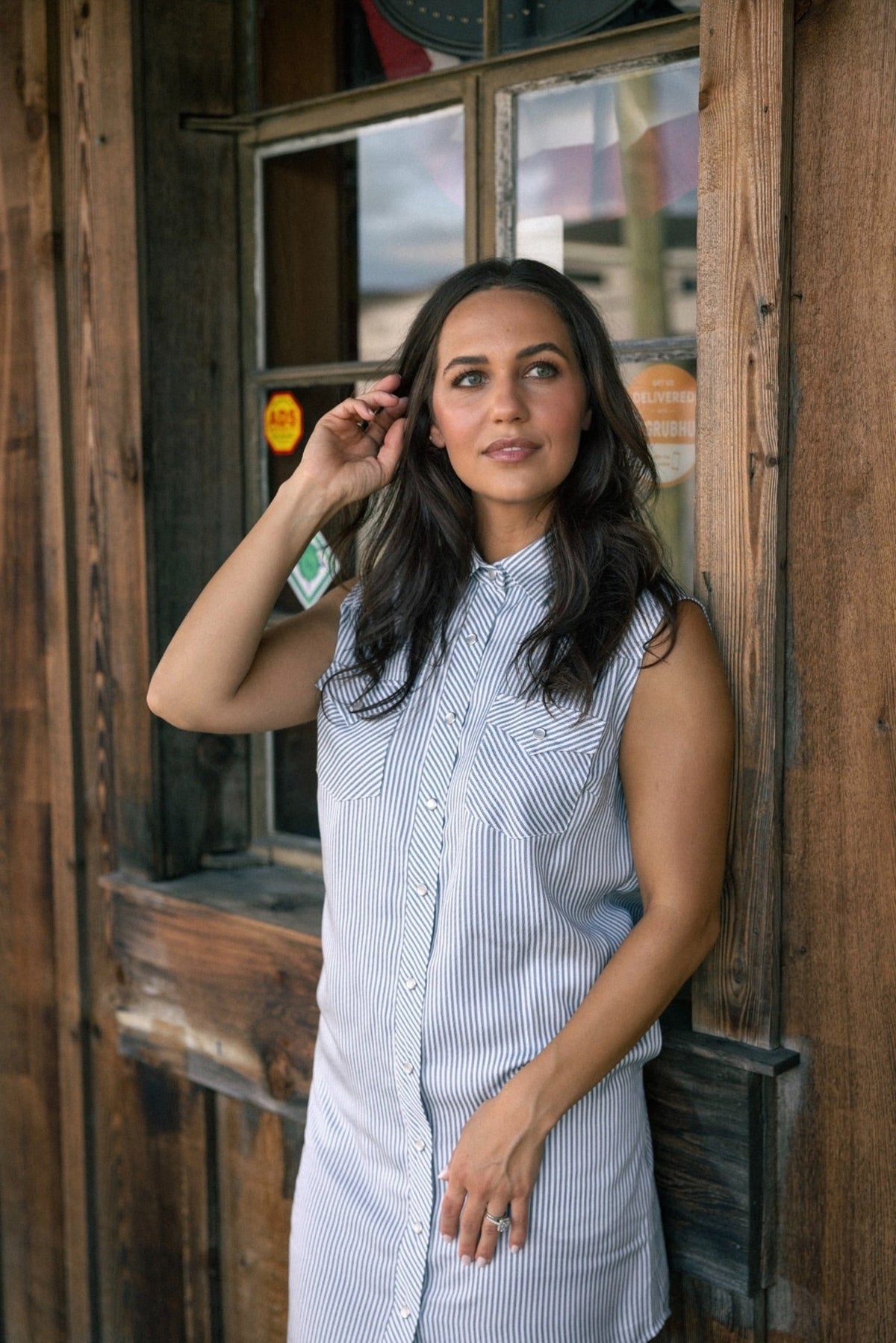 Woman in front of a rustic wooden storefront wearing the H Bar C Palm Beach striped sleeveless shirt dress.
