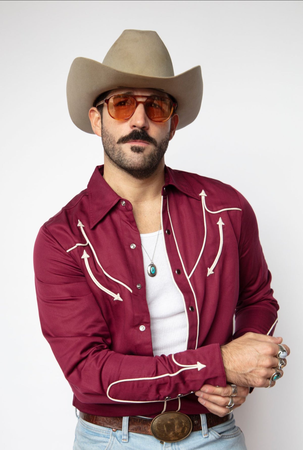 Man fastening the cuff of the H Bar C Reno maroon pearl snap shirt.