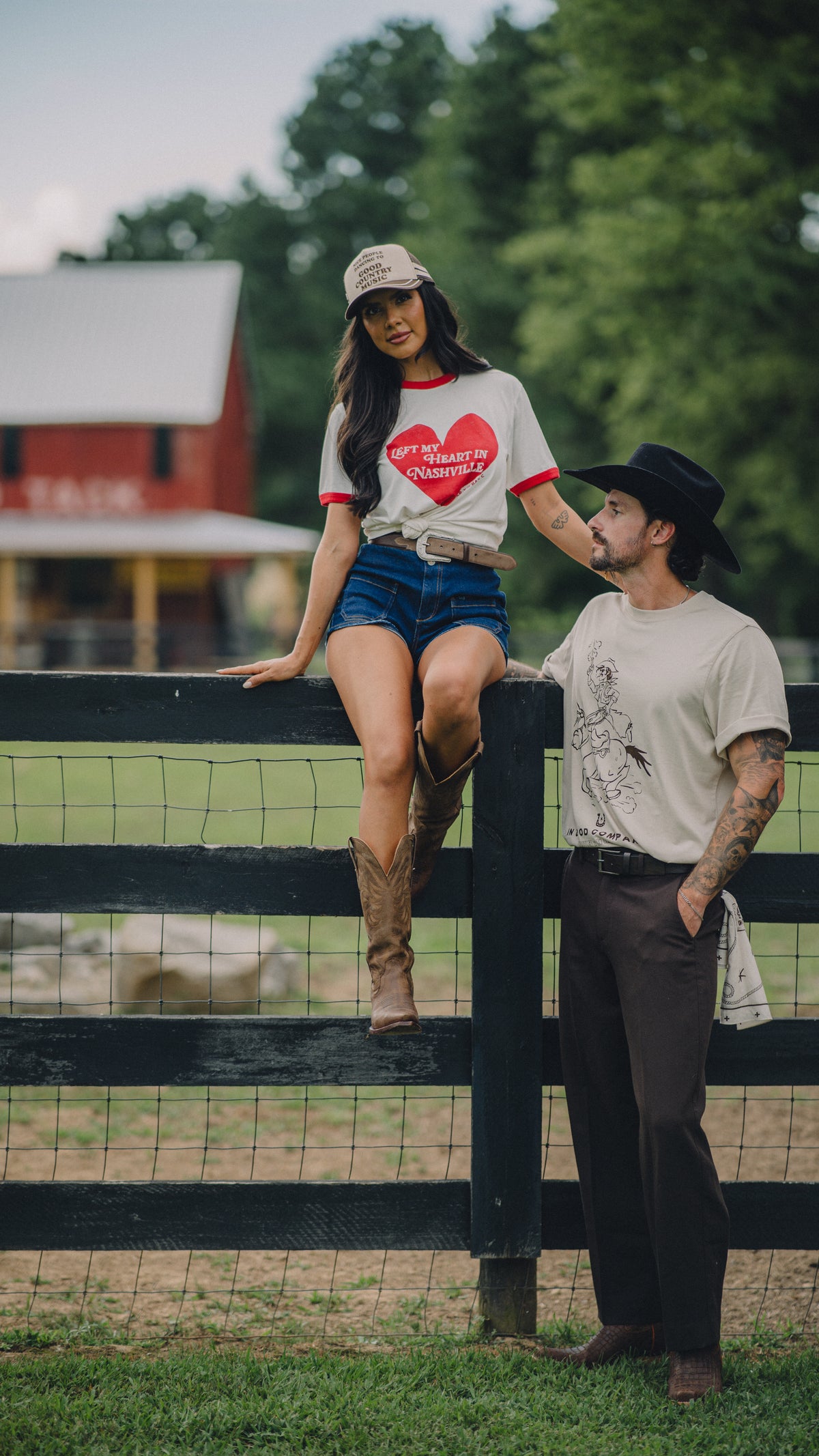 Woman sitting on a fence in the H Bar C x Rustler Left My Heart in Nashville tee with a cowboy outdoors.
