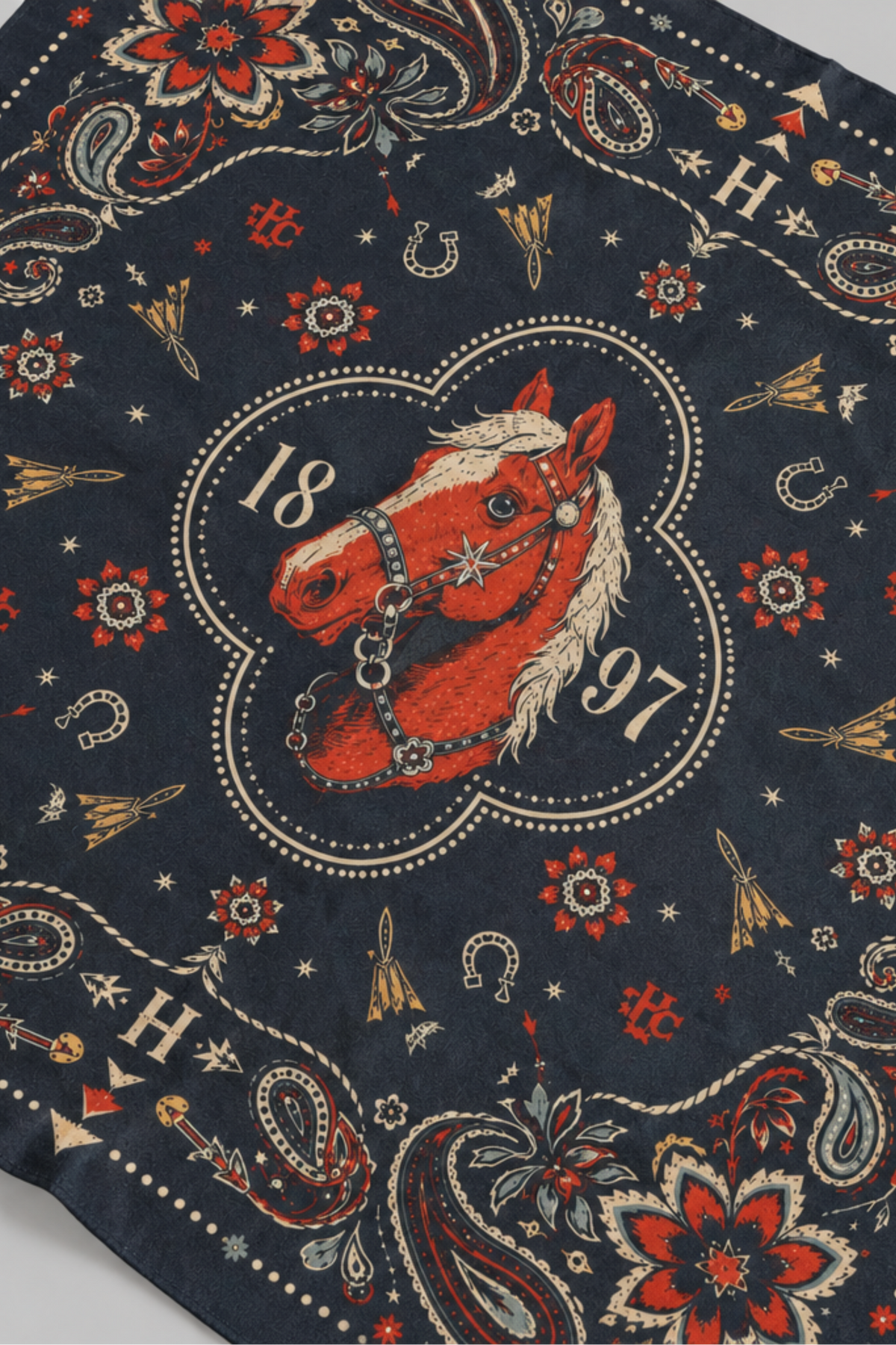 Close-up of the H Bar C Navy Floral Horse silk scarf center medallion: a chestnut horse head with bridle and the 1897 founding year, framed by red paisley.